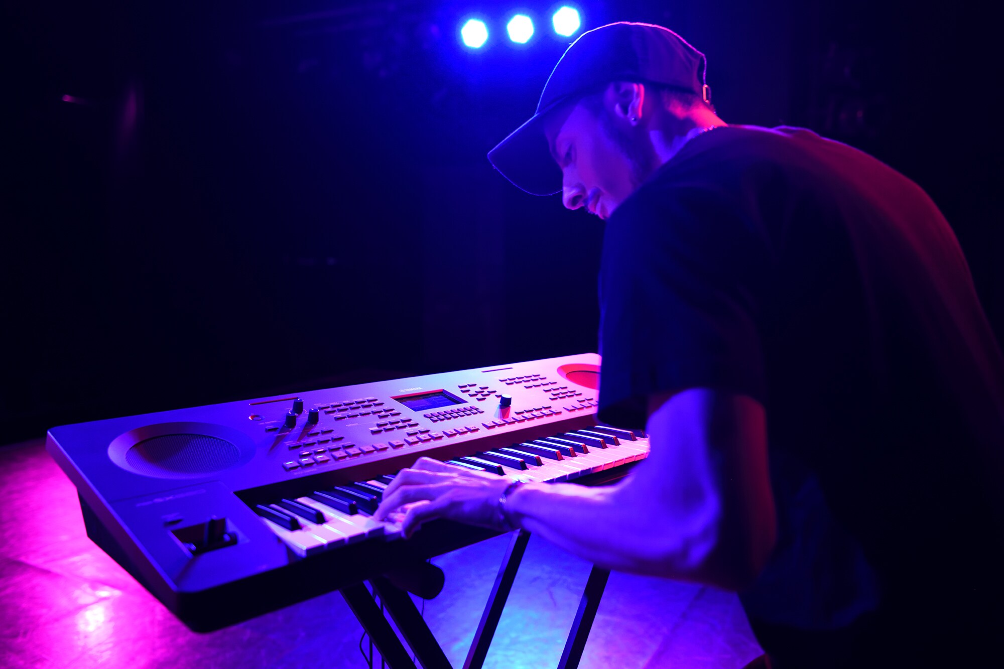 Una persona tocando un teclado Arranger Workstation Yamaha sobre un soporte bajo la iluminación del escenario
