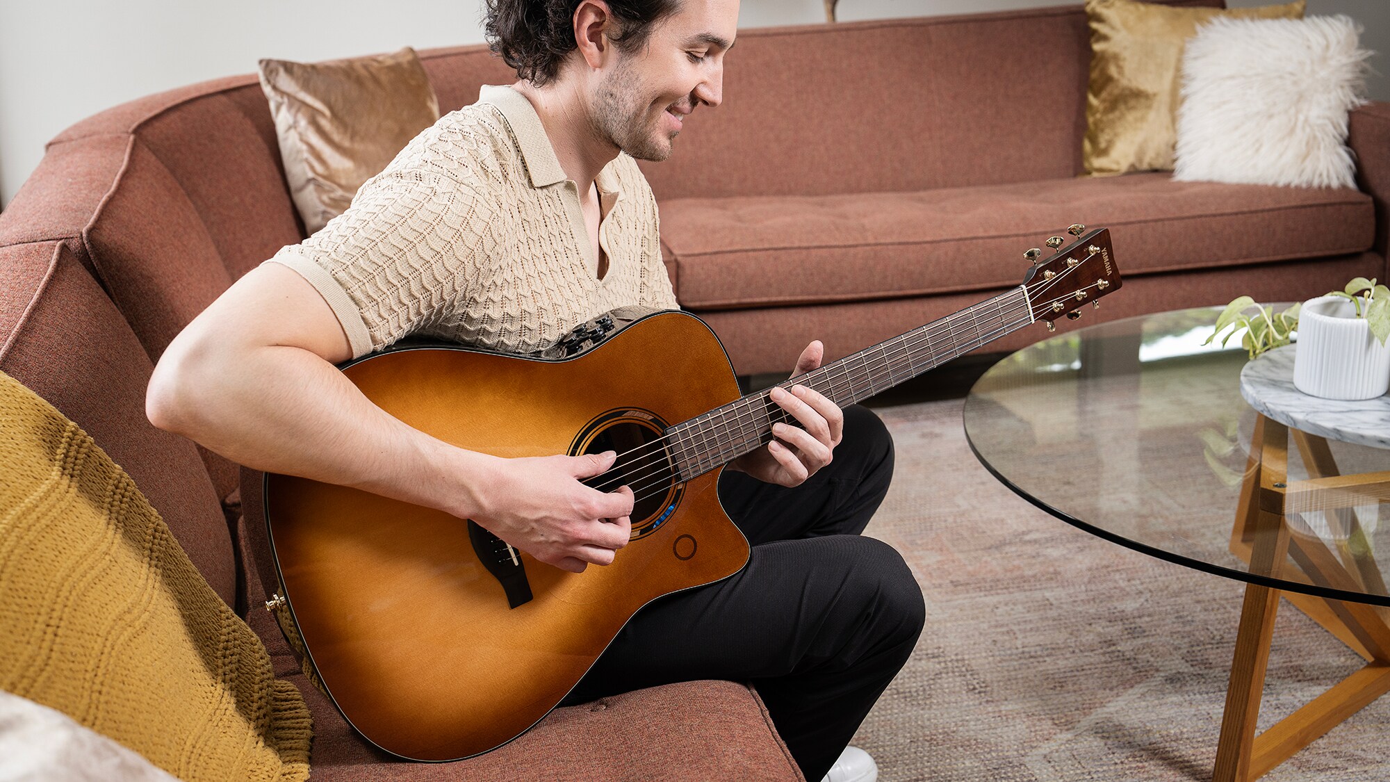Un hombre sentado en el sofá de un salón tocando una guitarra acústica TAG3 C