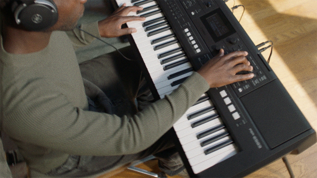 Persona tocando el teclado portátil Yamaha PSR-E483 con auriculares