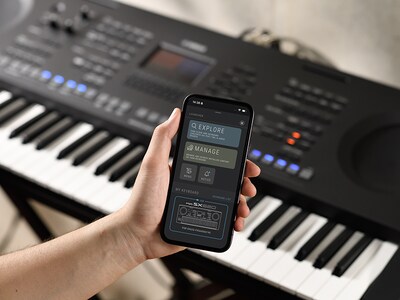 PSR-SX620 y una mano sosteniendo un smartphone con la pantalla de la aplicación oficial de Yamaha "Expansion Explorer".