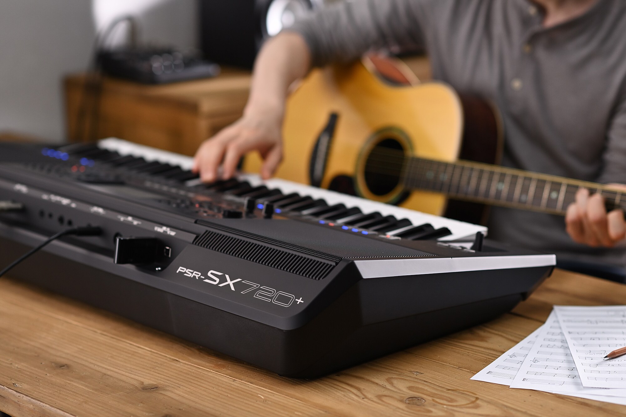 Foto de una persona tocando el Yamaha Arranger Workstation PSR‑SX720+ mientras sostiene una guitarra