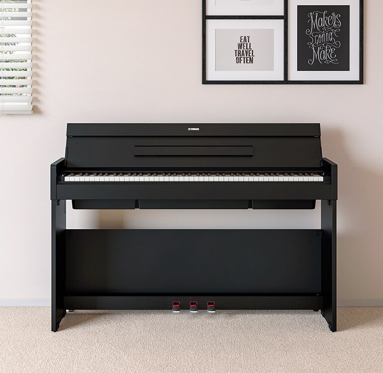 Un salón con un piano ARIUS negro situado junto a unas estanterías de pared con lámparas y un difusor, integrado de forma armoniosa en la decoración.