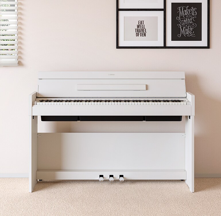 Un salón con un piano ARIUS blanco situado junto a unas estanterías de pared con lámparas y un difusor, integrado de forma armoniosa en la decoración.
